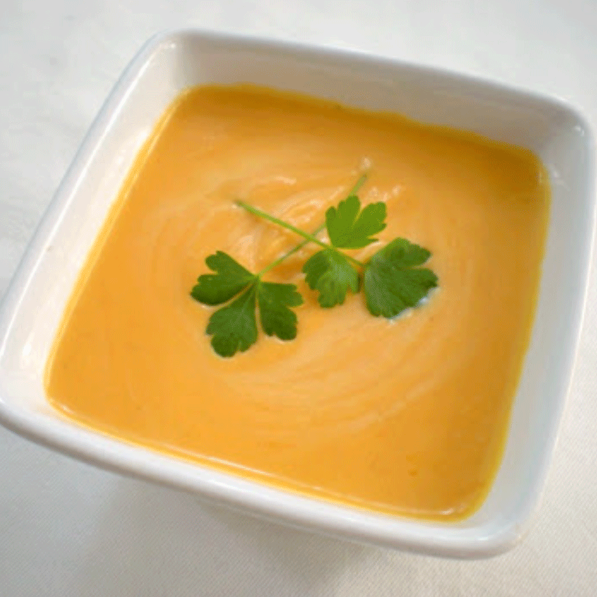Sweet potato soup in a white bowl topped with herbs